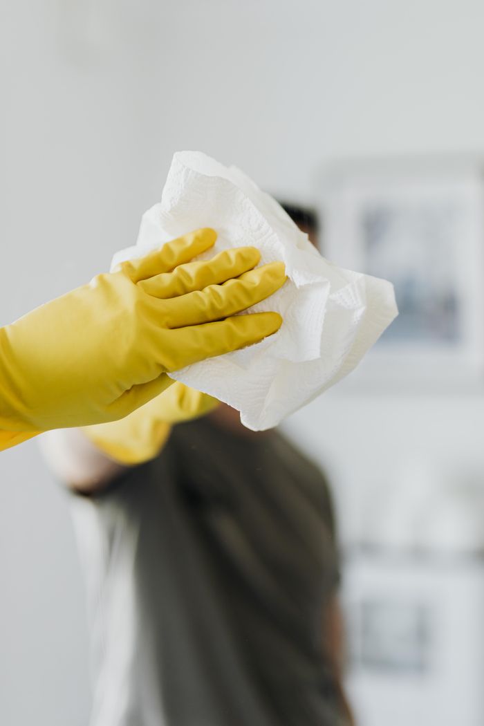 gallery-1 Anonymous male wearing yellow latex gloves and dark t shirt wiping mirror in bathroom with paper napkin