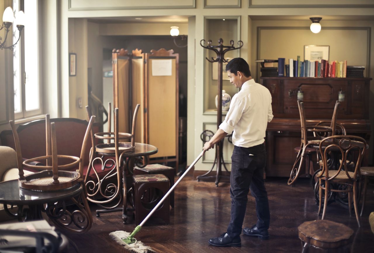 about-01 Side view of young ethnic male in uniform cleaning floor with mop while working in retro styled restaurant